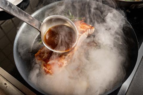 Kalbsrückensteak wird mit brauner Sauce abgelöscht, Dampf steigt aus der Pfanne